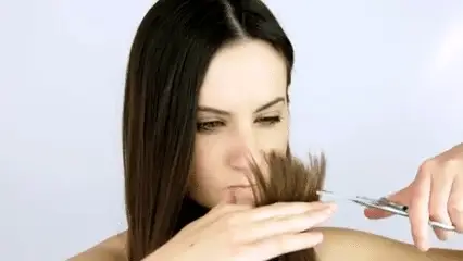 یک خانم که از موخوره موهای خود ناراضی است و در حال کوتاه کردن موهای خود با عصبانیت است